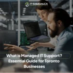 Two IT technicians reviewing code and security data on computer monitors in a dark server room.